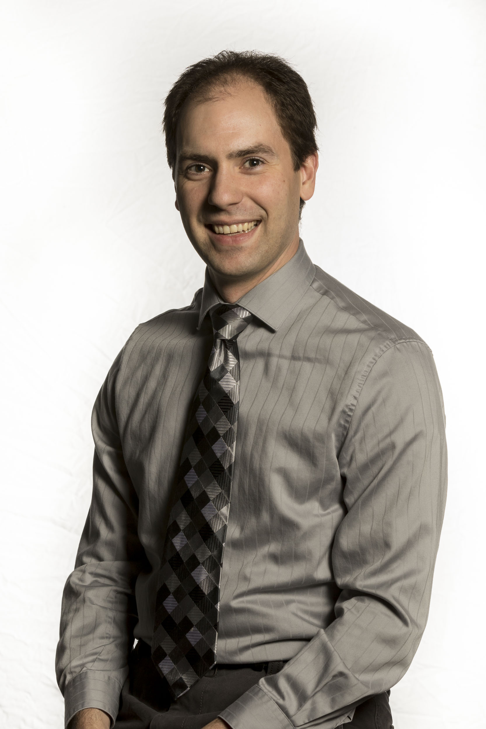 Photo of Matthew Collie smiling at the camera in a grey dress shirt and a grey and black tie.